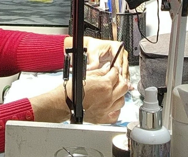 Manos de una técnica trabajando las uñas de una clienta en la mesa de manicura